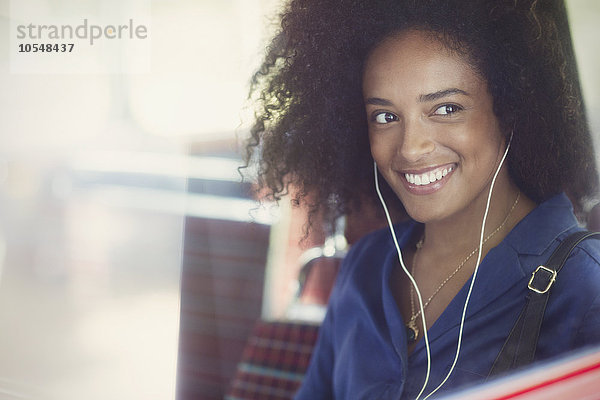 Lächelnde Frau mit Afro Musik hören mit Kopfhörer im Bus