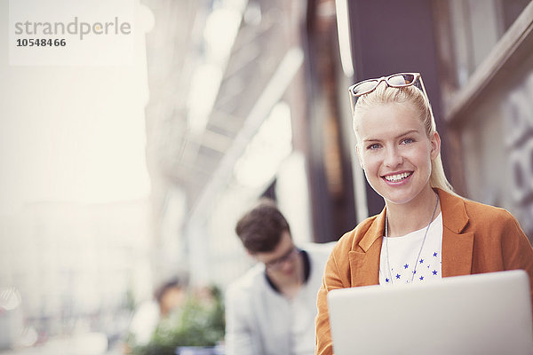 Portrait lächelnde blonde Frau mit Laptop auf dem Bürgersteig Cafe