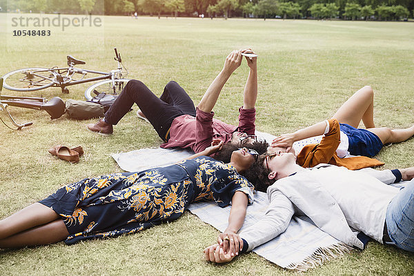 Freunde entspannen sich und nehmen Selfie im Kreis auf Decke in Park