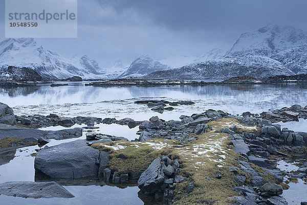 Schneebedeckte Berge hinter kalter  ruhiger Bucht  Lofoten Inseln  Norwegen