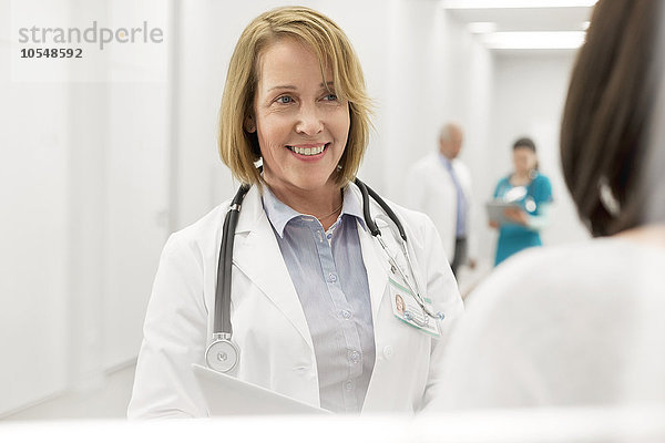 Lächelnder Arzt im Gespräch mit dem Patienten im Krankenhauskorridor