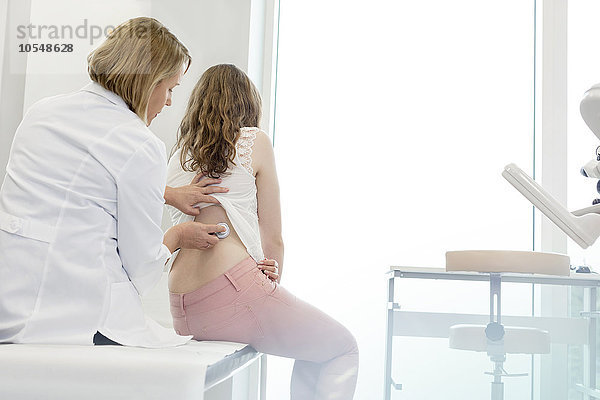 Arzt mit Stethoskop auf dem Rücken eines jugendlichen Patienten im Untersuchungsraum