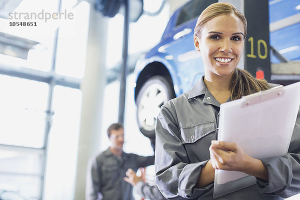 Portrait lächelnder Mechaniker mit Klemmbrett in der Autowerkstatt