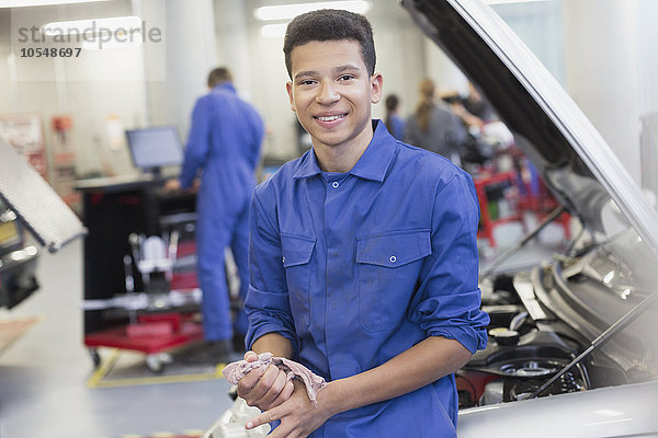 Porträt eines lächelnden Mechanikers  der sich in der Autowerkstatt auf das Auto stützt.