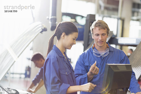 Mechaniker diskutieren Teil am Computer in der Kfz-Werkstatt