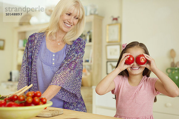 Portrait verspielte Enkelin  die in der Küche die Augen mit Tomaten bedeckt