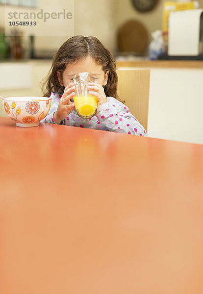 Mädchen trinkt Orangensaft am Frühstückstisch