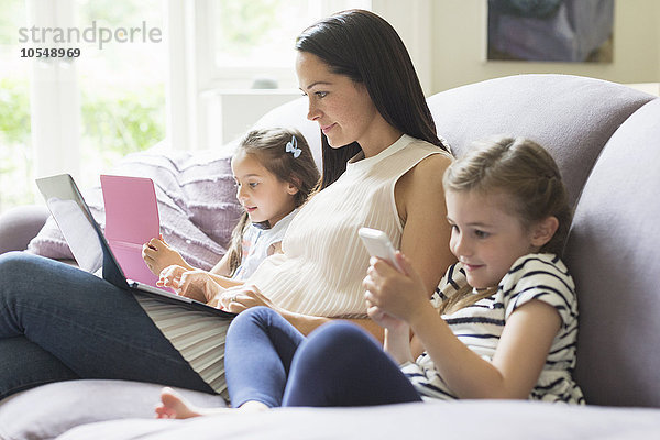 Mutter und Töchter mit Laptop  Handy und digitalem Tablett auf Sofa