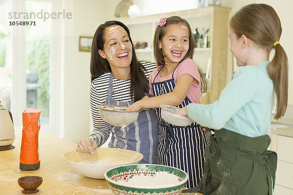 Lachende Mutter und Töchter beim Backen mit Mehl auf den Gesichtern in der Küche