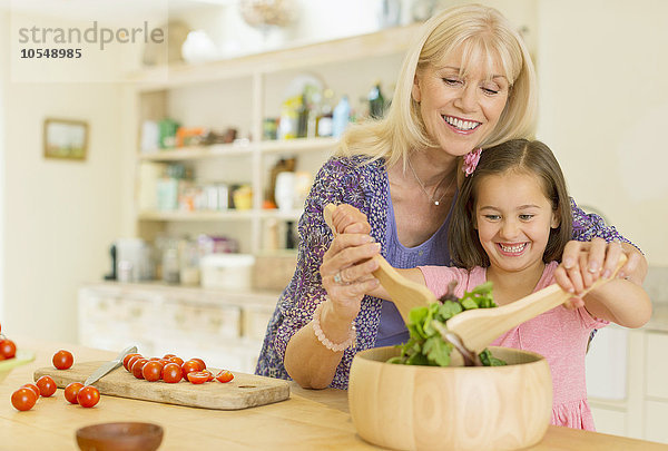 Großmutter und Enkelin beim Salatwerfen in der Küche