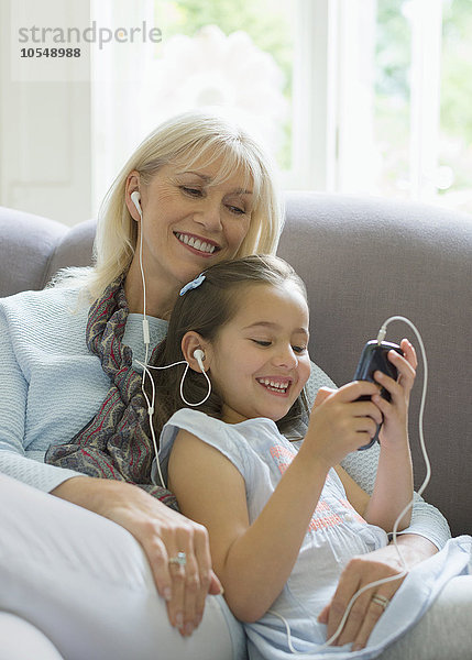 Großmutter und Enkelin teilen sich Kopfhörer und hören Musik auf dem Sofa.