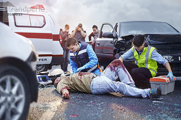 Rettungskräfte neigen zu blutigen Autounfallopfern auf der Straße