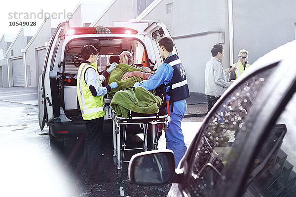 Rettungskräfte  die das Opfer eines Autounfalls auf der Krankentrage hinter dem Krankenwagen betreuen.