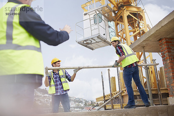 Bauarbeiter heben auf der Baustelle Metallmast unter den Kran