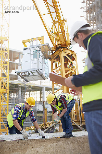 Bauarbeiter mit ebenem Werkzeug unter dem Kran auf der Baustelle