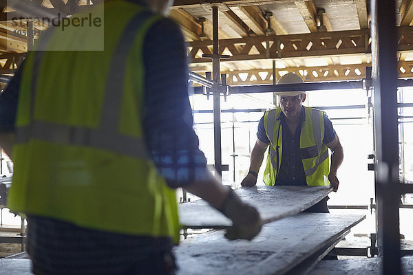 Bauarbeiter beim Heben von Sperrholz auf der Baustelle