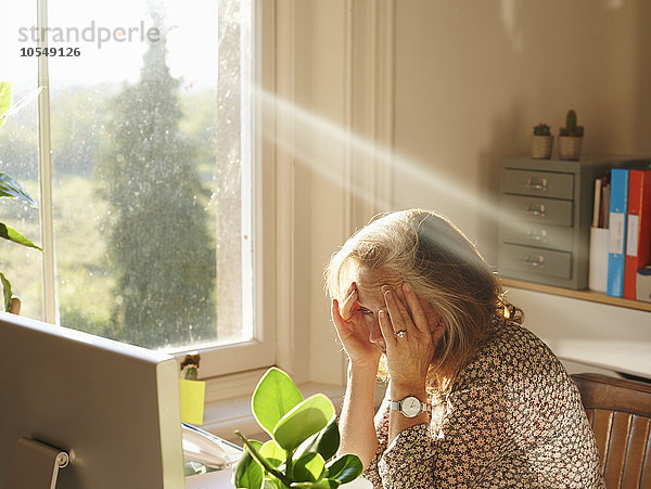 Gestresste Frau mit Computer im sonnigen Home-Office