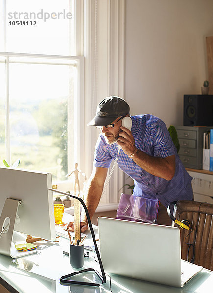 Mann am Telefon und Computer am Schreibtisch im sonnigen Home-Office