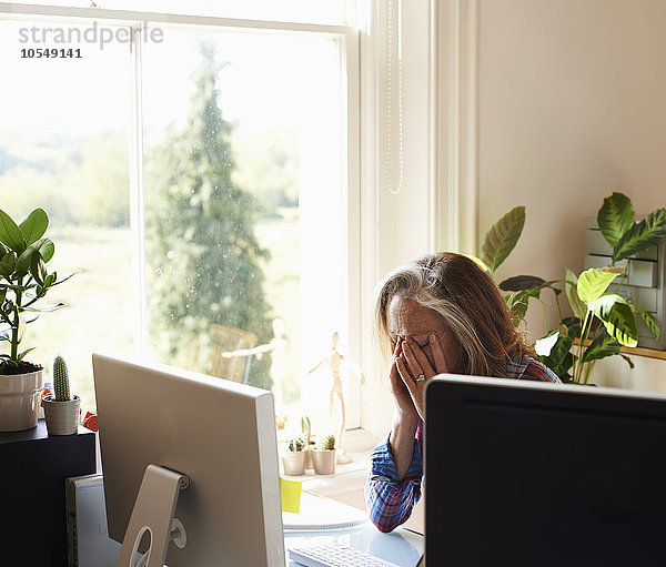 Müde Frau mit Kopf in den Händen am Computer im Home Office