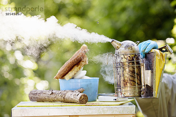 Ein Imker hält einen Metallraucher  der Rauch über die Spitze eines Bienenstocks bläst.