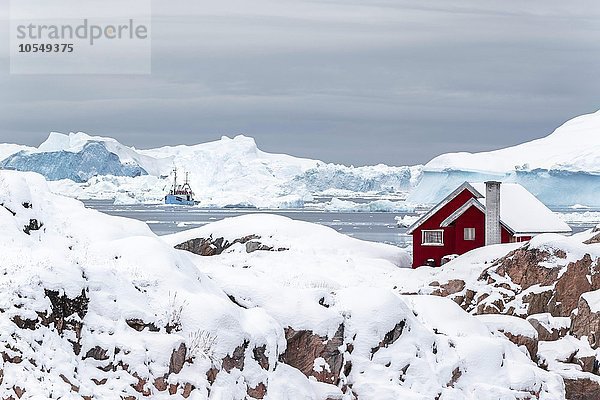 Rote grönländische Hütte  Haus auf einer Halbinsel  vor großen Eisbergen mit Fischerboot  Ilulisaat  Grönland  Nordamerika