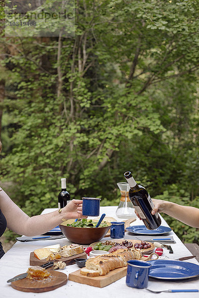 Tisch in einem mit Tellern und Speisen gedeckten Garten  ein Mann schenkt ein Glas Wein ein.