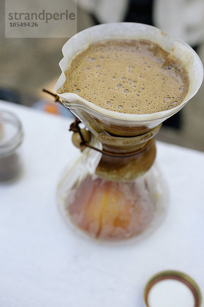 Hochwinkelansicht einer Glas-Kaffeemaschine und Filterpapier mit Kaffee- und Wasserfilterung durch