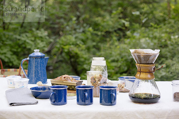 Tisch in einem Garten  mit Kaffeemaschine  Tassen und Schalen  einem Kuchen und Müsli.