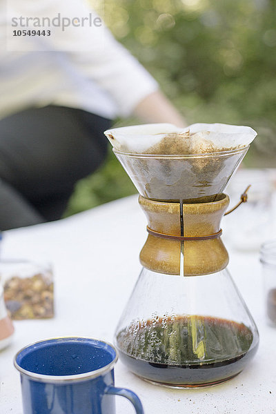 Nahaufnahme einer gläsernen Kaffeemaschine auf einem Tisch in einem Garten.