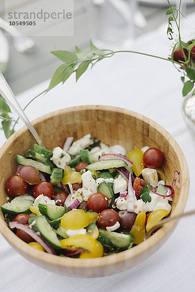 Eine Schüssel Salat auf einem Tisch in einem Garten mit frischen Tomaten  Gurken und Paprika.