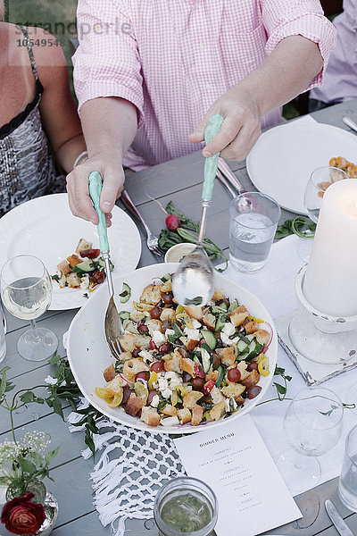 Menschen um einen Tisch bei einer Gartenparty  eine Schüssel Salat.