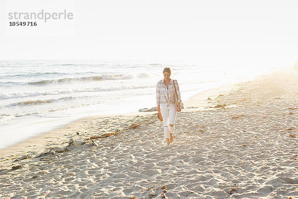 Frau geht an einem Sandstrand am Meer entlang.