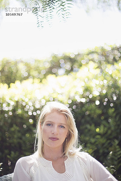 Porträt einer blonden Frau  die in einem Garten steht.