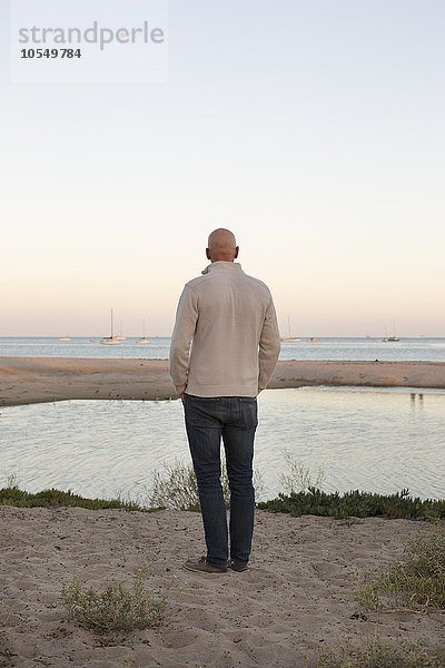 Kahlköpfiger Mann  der an einem Sandstrand am Meer steht.