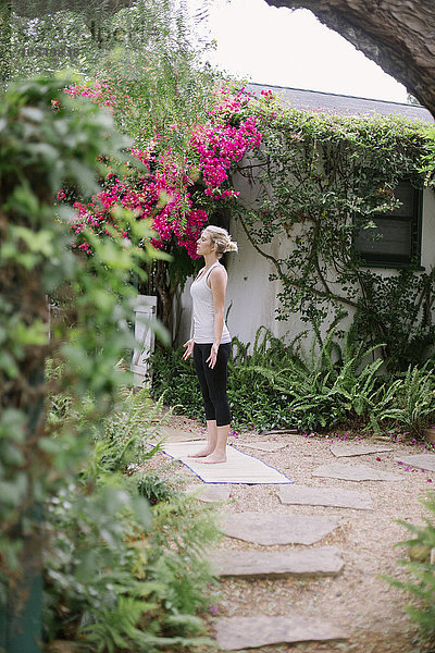 Blonde Frau beim Yoga in einem Garten.