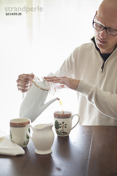 Mann  der an einem Tisch sitzt und sich eine Tasse Kaffee einschenkt.