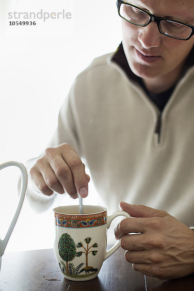 Mann  der an einem Tisch sitzt und eine Tasse Kaffee umrührt.