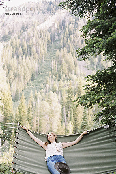 Frau entspannt sich in einer großen Hängematte in einem Wald.