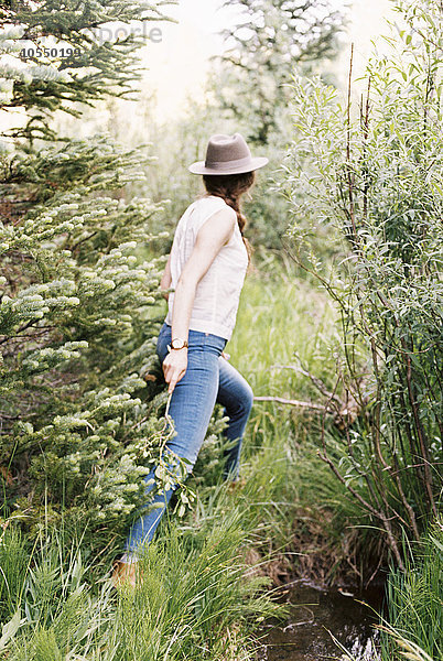 Frau in Jeans und mit Hut  die durch einen Wald geht.