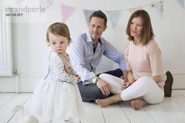 Ehepaar mit ihrer kleinen Tochter  die im Fotografenstudio auf dem Boden sitzt und für ein Bild posiert.