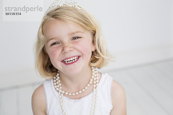 Junges Mädchen  das ein Diadem und eine Perlenkette trägt und für ein Bild in einem Fotostudio posiert.