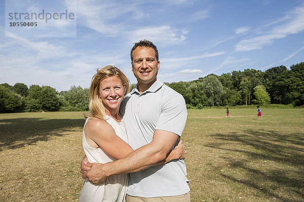 Ein Paar steht in einem Park  lächelt und umarmt sich.