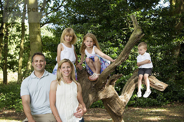 Familie mit drei Kindern an einem Baum in einem Wald  die für ein Bild posieren.