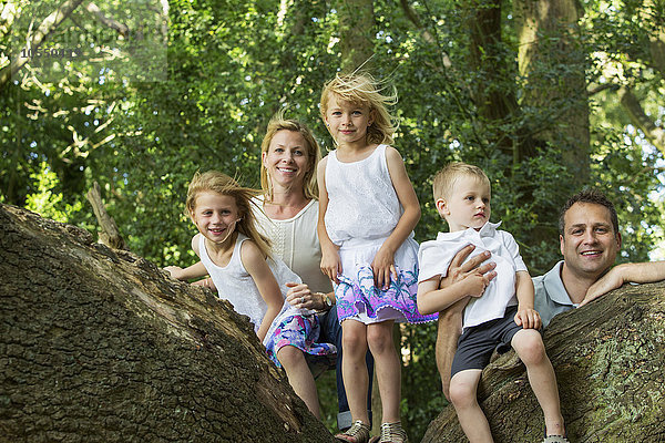 Familie mit drei Kindern an einem Baum in einem Wald  die für ein Bild posieren.