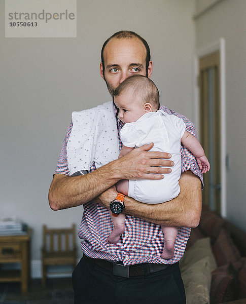 Ein Mann hält ein junges Baby nahe an seiner Brust.