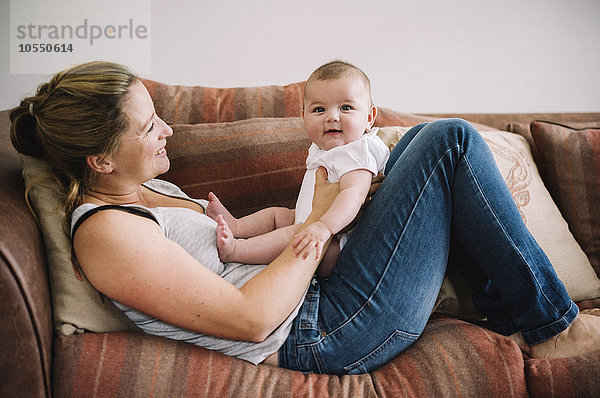 Eine Frau liegt auf einem Sofa und spielt mit einem kleinen Mädchen.