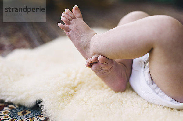 Ein Baby  das auf einem Schafsfellteppich liegt und gegen die Beine tritt.