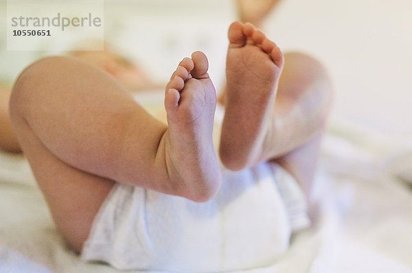 Ein Baby  das auf einem Schafsfellteppich liegt und gegen die Beine tritt.