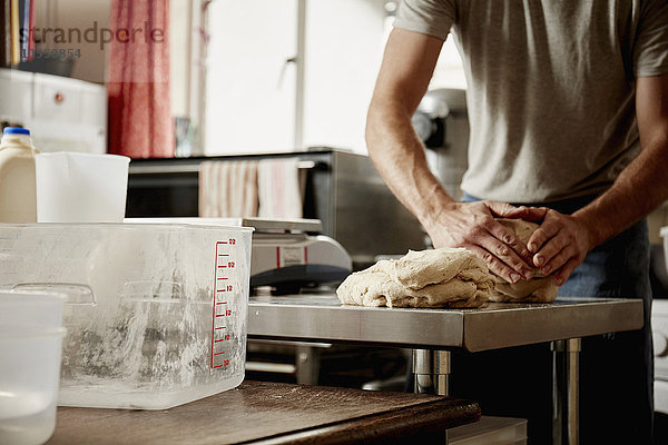 Ein Mann  ein Bäcker  der in einer Großküche arbeitet und ein großes Stück Teig knetet.