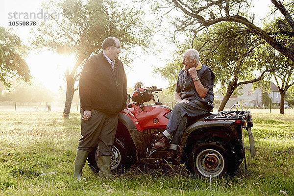 Zwei Männer  ein Landwirt und ein Mann mit einem Klemmbrett  mit einem Quad in einem Obstgarten.